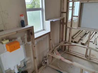 Bathroom timber framing with plumbing rough-in, orange junction box, window sill, and cistern support.